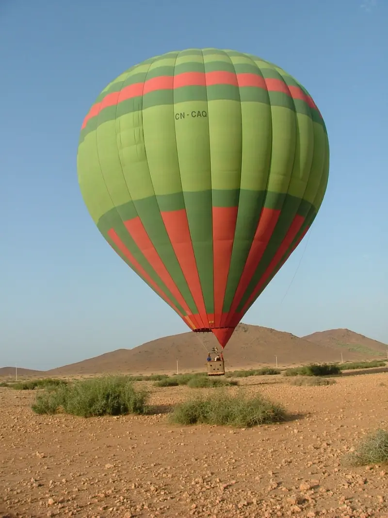 A green and red hot air balloon rising above the hills near Marrakech